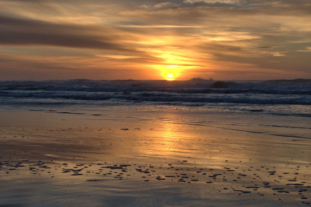 Waves crash into the air in front of the setting sun