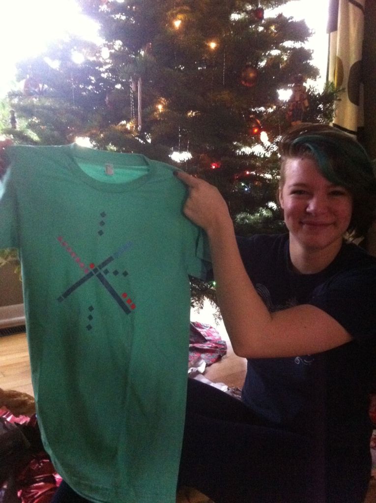 Gift time! Tara's holding a T-shirt with the pattern of the Portland International Airport carpet.